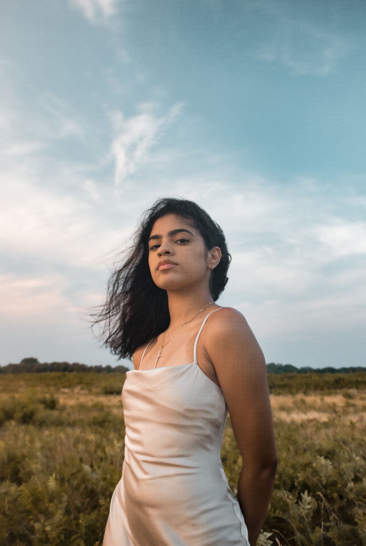 Woman in a satin slip dress standing in a field under a blue sky
